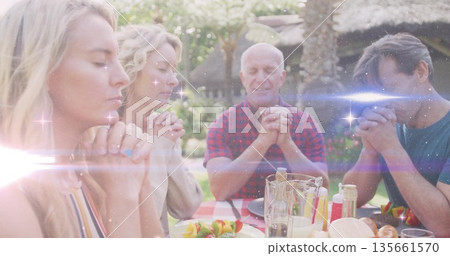 Praying family bowing heads and clasping hands around checkered table in garden, with skewers Praying family bowing heads and clasping hands around checkered table in garden, with skewers 135661570