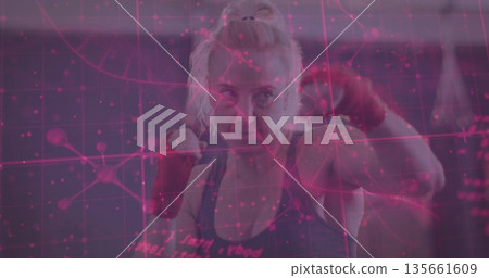 Practicing boxer throwing punches inside gym with punching bag and red wraps, digital grid overlay 135661609