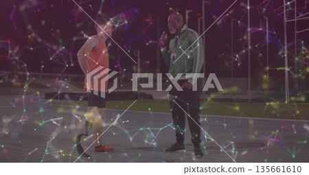 Coach interviewing athlete in sportswear on track at night with microphone and prosthetic blade Coach interviewing athlete in sportswear on track at night with microphone and prosthetic blade 135661610