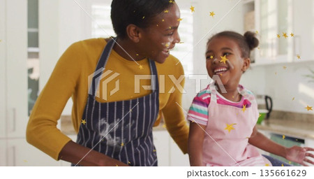 Laughing mother and daughter in striped and pink aprons using mixing bowl at home kitchen counter Laughing mother and daughter in striped and pink aprons using mixing bowl at home kitchen counter 135661629
