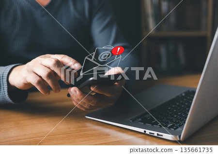 person using a smartphone receives a digital email notification with an alert symbol, representing spam, phishing, fake messages, scams, hacked accounts, malware, red warning alert, and virus threats. person using a smartphone receives a digital email notification with an alert symbol, representing spam, phishing, fake messages, scams, hacked accounts, malware, red warning alert, and virus threats. 135661735