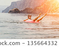 Woman sea inflatable laughing while floating on a pink ring in the ocean near rocky cliffs during sunset 135664332