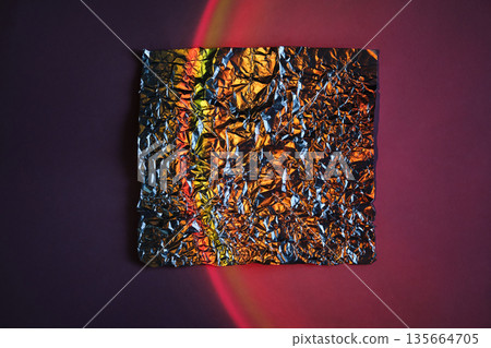 Crumpled metallic foil square on abstract neon gradient background with red light arc Crumpled metallic foil square on abstract neon gradient background with red light arc 135664705