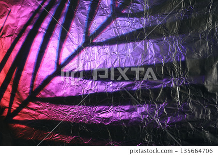 Palm leaf shadow on crumpled metallic foil with purple and pink neon light reflections 135664706