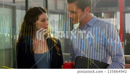 Two professionals reviewing data chart overlay in office, holding red coffee mug and closed laptop Two professionals reviewing data chart overlay in office, holding red coffee mug and closed laptop 135664942