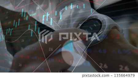 Interacting business-clad woman adjusting round-faced smartwatch at office desk, with market graphs 135664979