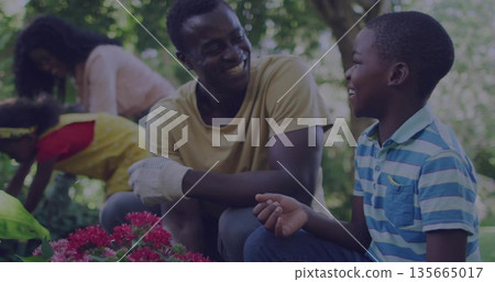 Smiling dad and son kneeling examining pink blossoms in backyard, with gloves and tray Smiling dad and son kneeling examining pink blossoms in backyard, with gloves and tray 135665017