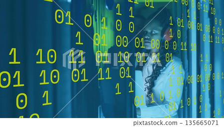 IT technician in white shirt red headset checking controls in DC aisle, binary overlay, copy space 135665071