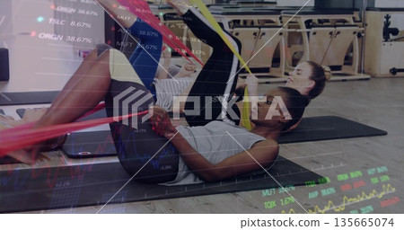Woman in sportswear pulling resistance band around thighs on yoga mat in gym, with phone 135665074