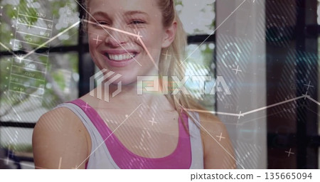 Smiling athletic woman wearing sportswear, scanning metrics at fitness studio with digital overlays Smiling athletic woman wearing sportswear, scanning metrics at fitness studio with digital overlays 135665094