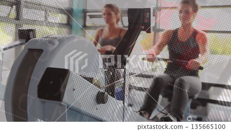 Rowing woman on ergometer monitoring digital display while gripping handlebars at fitness studio Rowing woman on ergometer monitoring digital display while gripping handlebars at fitness studio 135665100
