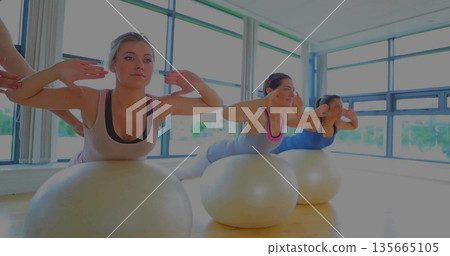 Performing back extensions three women on stability balls in fitness studio, trees outside 135665105