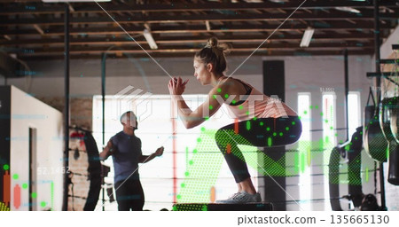 Crouching woman athlete performing squat on plyometric box in brick gym, with digital data overlay Crouching woman athlete performing squat on plyometric box in brick gym, with digital data overlay 135665130