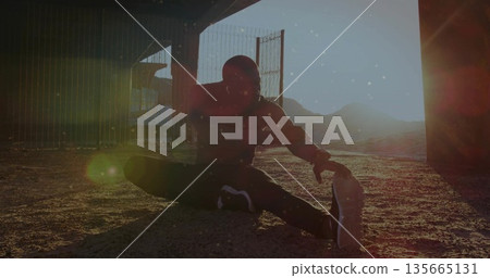 Stretching man in hoodie, running shoes, reaching toward foot under overpass, with chain link fence Stretching man in hoodie, running shoes, reaching toward foot under overpass, with chain link fence 135665131