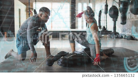 Kneeling trainer guiding client pressing heavy bag in boxing gym with hand wraps, financial charts Kneeling trainer guiding client pressing heavy bag in boxing gym with hand wraps, financial charts 135665132