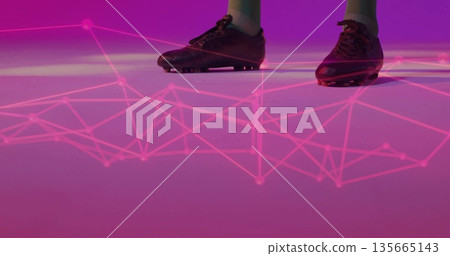 Standing male wearing black soccer cleats and athletic socks in studio, with glowing pink network 135665143
