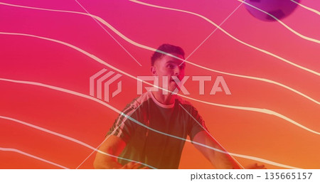 Pedaling male enthusiast wearing green sports shirt on stationary bike in studio, with neon streaks 135665157