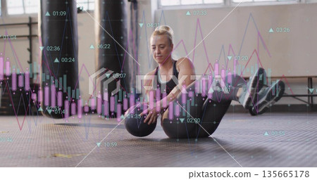 Doing V-sit core exercise female athlete lifting medicine ball at gym studio, with chart overlay 135665178