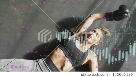Lying athlete wearing bra, leggings, boxing gloves, raising arm on mat showing financial charts Lying athlete wearing bra, leggings, boxing gloves, raising arm on mat showing financial charts 135665186