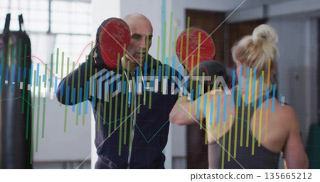 Trainee in sportswear throwing punches in gym, with trainer holding focus mitts, chart overlay 135665212