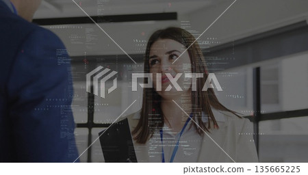 Woman in beige blazer holding clipboard and briefing colleague in office, with blue lanyard Woman in beige blazer holding clipboard and briefing colleague in office, with blue lanyard 135665225