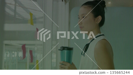 Holding mug, Asian woman wearing blouse gazing at glass office wall with sticky notes, copy space 135665244