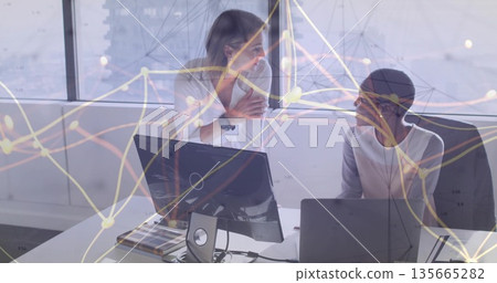 Collaborating two mid adult women analyzing network data at modern office, with desktop monitor 135665282