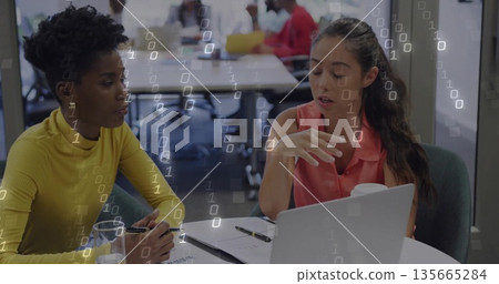 Discussing project details women sitting at table in open-plan office with laptop and documents Discussing project details women sitting at table in open-plan office with laptop and documents 135665284