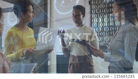 Collaborating three women presenting data on holographic display in office, with laptop and tablet 135665285