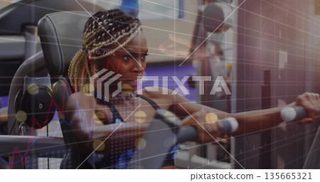 Gripping woman in sports bra pushing chest press machine at gym, with braided hair Gripping woman in sports bra pushing chest press machine at gym, with braided hair 135665321