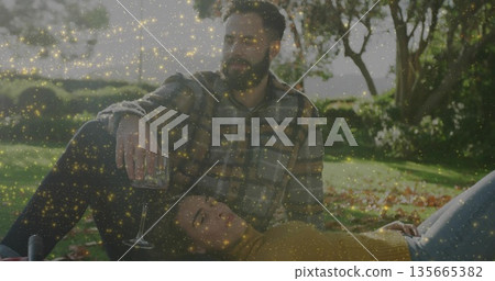 Bearded man in plaid shirt, woman in mustard sweater reclining in garden, with wine glass, bottle 135665382
