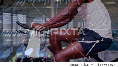 Riding male athlete in sportswear pedaling stationary bike in modern gym, with digital metrics Riding male athlete in sportswear pedaling stationary bike in modern gym, with digital metrics 135665398