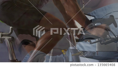 Pedaling male participant on exercise bike in fitness studio with trainer adjusting resistance knob 135665408
