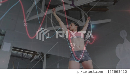 Suspending athlete wearing sports bra, shorts on aerial hoop in gym, with rigging, waveform overlay Suspending athlete wearing sports bra, shorts on aerial hoop in gym, with rigging, waveform overlay 135665410