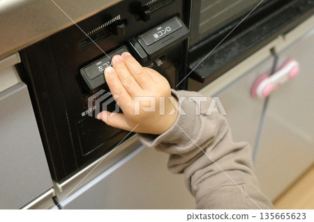 A toddler touching the switch on a gas stove in the kitchen A toddler touching the switch on a gas stove in the kitchen 135665623