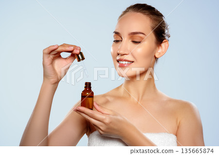 Woman applying serum in bright setting with brown glass dropper bottle in hand 135665874
