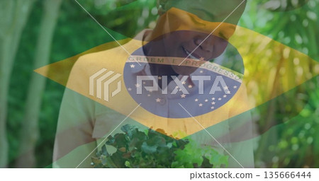 Woman holding leafy greens in tropical garden, wearing headscarf, shirt with Brazilian flag overlay 135666444