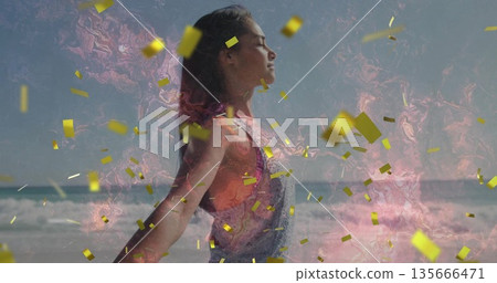 Standing woman wearing orange top in overalls, closing eyes on beach, golden confetti, pink swirl 135666471