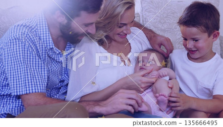 Leaning parents watching boy reaching toward baby on light sofa in living room, with cushions Leaning parents watching boy reaching toward baby on light sofa in living room, with cushions 135666495