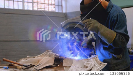 Welding technician welding car panel on garage workbench, with welding torch and helmet, copy space 135666556