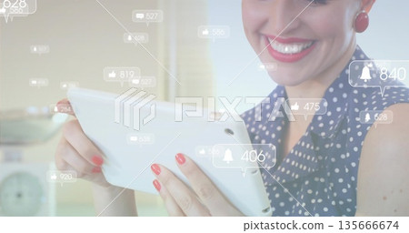 Smiling woman wearing navy blouse interacting with tablet in home kitchen, with notification icons Smiling woman wearing navy blouse interacting with tablet in home kitchen, with notification icons 135666674