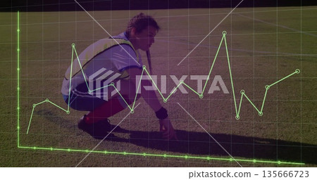 Squatting athlete wearing yellow bib red socks shin guards on grass field, with green grid overlay 135666723