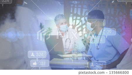 Discussing cases, doctors in scrubs and lab coat reviewing laptop in conference room, with papers 135666800