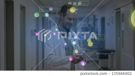 Doctor in lab coat with stethoscope examining smartphone in hospital hall, with chat icons floating 135666802