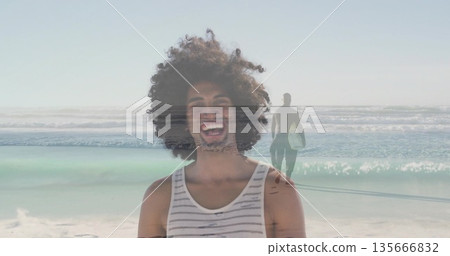 Smiling man wearing striped tank top on beach, with second man walking into surf holding longboard Smiling man wearing striped tank top on beach, with second man walking into surf holding longboard 135666832