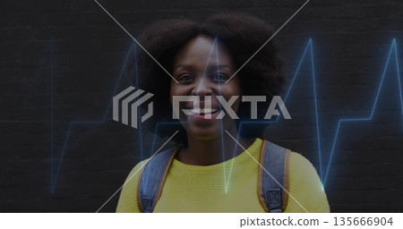 Smiling woman in yellow sweater posing against brick alley wall, with backpack, blue EKG overlay 135666904