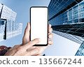 Mobile Phone Screen Mockup Held in Hand Against Towering Downtown Skyscrapers 135667244
