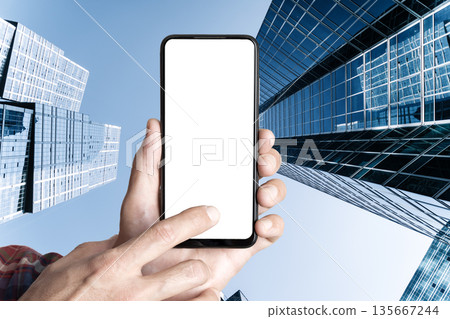 Mobile Phone Screen Mockup Held in Hand Against Towering Downtown Skyscrapers Mobile Phone Screen Mockup Held in Hand Against Towering Downtown Skyscrapers 135667244