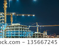 Construction Site at Night with Illuminated Tower Cranes and Building Skeletons 135667245