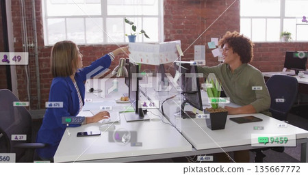 Handing printed chart, coworkers wearing business wear working at office desk with acrylic divider Handing printed chart, coworkers wearing business wear working at office desk with acrylic divider 135667772
